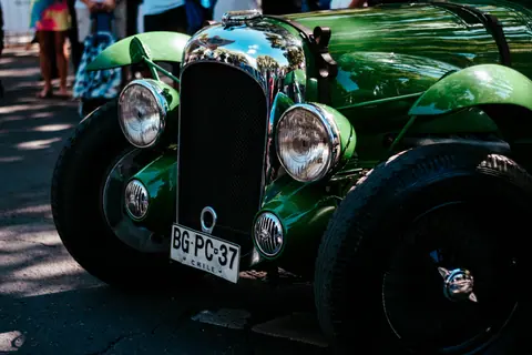 Close up of a classic green vintage car showcasing headlights and license plate, parked outdoors.