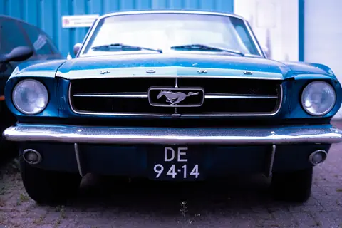 Front view of a classic blue Ford Mustang car parked outdoors.