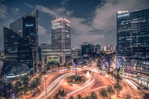 Stunning nighttime long exposure of Mexico City's bustling traffic circle with illuminated skyscrapers.