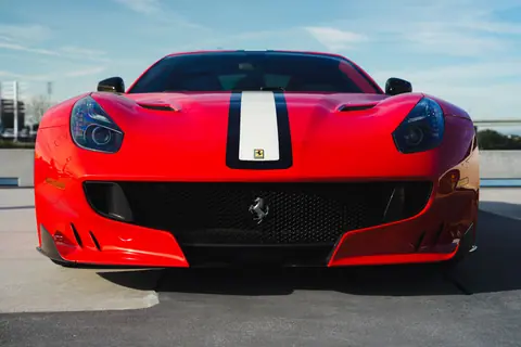 Front view of a sleek red sports car with a racing stripe on a sunny day.