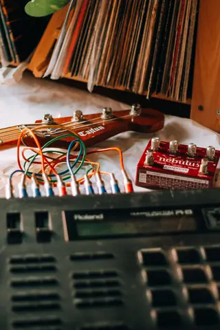 Close-up of electronic music gear with a guitar neck and colorful cables, ideal for music production themes.