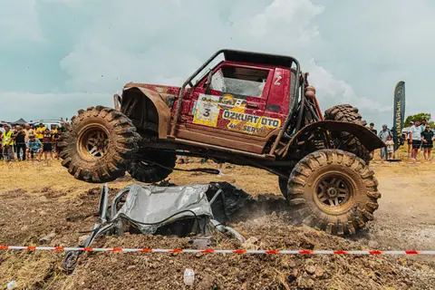 Exciting offroad monster truck jumping over crushed car at outdoor racing event. Adrenaline-filled adventure.