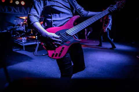 A performer playing bass guitar on stage in a vibrant concert setting.