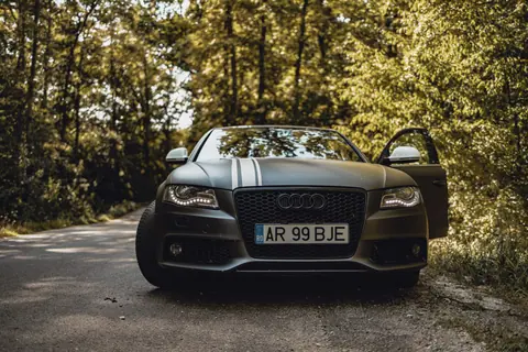 Front view of a black Audi car on a forest road with an open door.