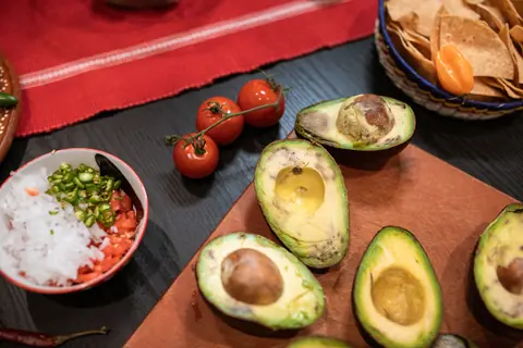 Overhead view of avocados, tomatoes, and toppings for making fresh guacamole.
