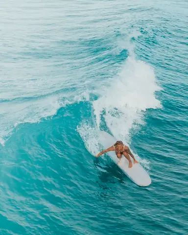 Dynamic aerial shot of a woman surfing on stunning turquoise ocean waves, capturing the thrill of the sport.