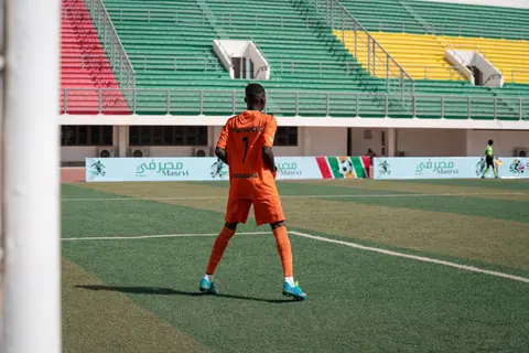 Soccer player in orange uniform on colorful stadium field during daytime game.