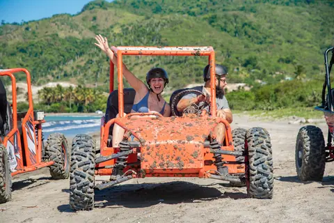 Two adults enjoying an exciting dune buggy ride on a sunny day near the beach.
