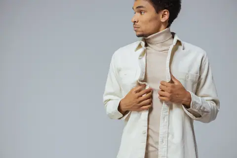 Man posing in neutral turtleneck and dress shirt with hands on collar, looking sideways.