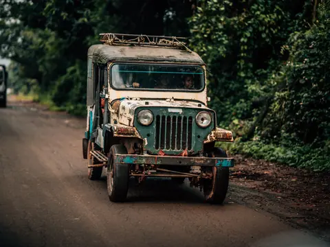 A classic vintage jeep navigates a rural road in the lush landscapes of Koraput, India.