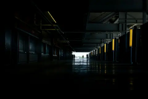 A long, dark industrial corridor with silhouetted figures in the distance, creating a moody atmosphere.