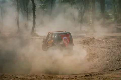 Off-road vehicle with Turkish flag driving through a dusty forest course.