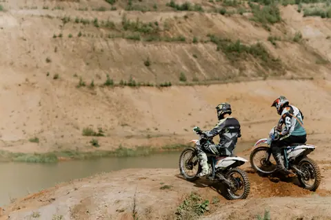 Two riders enjoy dirt biking on a cliffside overlooking a scenic river in summer.