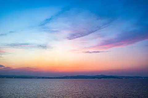 Stunning view of a colorful sunset over the ocean with city lights in the distance. Perfect for travel and nature enthusiasts.