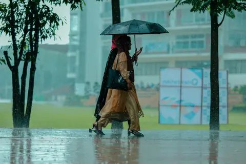 Two women in traditional attire walking under an umbrella during rainy weather.