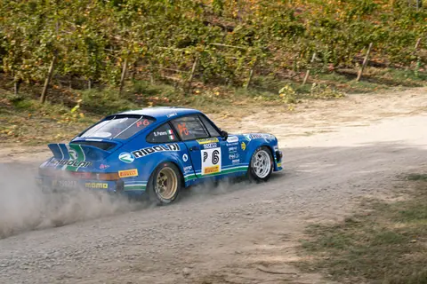 A thrilling rally car speeds on a dirt track in San Marino's scenic landscape.