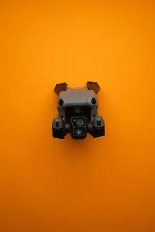 Close-up of a modern compact drone against a bright orange background, showcasing drone technology.