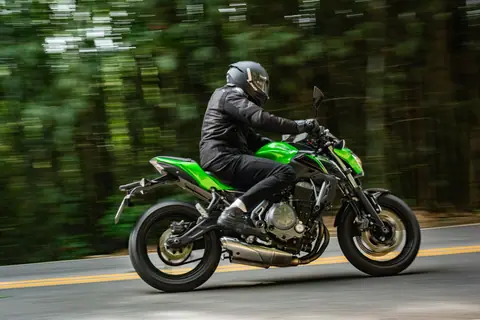 A biker in full gear rides a green motorcycle through a forested road, showcasing speed and adventure.