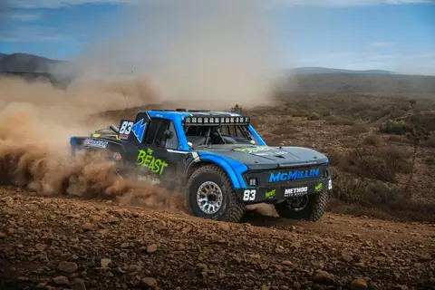 Blue truck kicking up dust during thrilling desert race in Baja California.