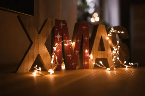 Xmas sign adorned with glowing fairy lights, creating a warm festive atmosphere indoors.