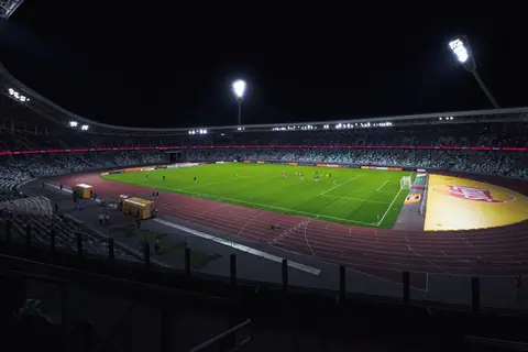 Brightly lit empty soccer stadium with green field under spotlights during night time.
