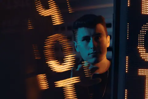 Artistic portrait of a man in front of a glowing neon sign, creating a dramatic mood.