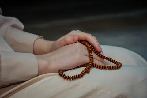 Close-up of hands holding wooden prayer beads, symbolizing spirituality and meditation.