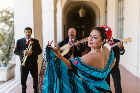 Smiling Mexican dancer in traditional blue dress performing with mariachi band indoors.