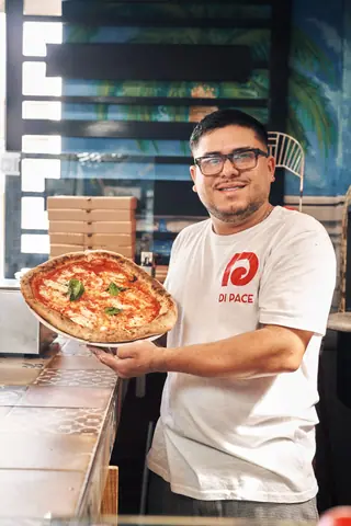 Smiling chef presents a freshly baked pizza in an indoor pizzeria setting.