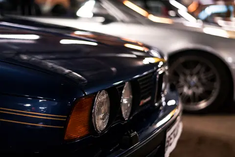 Close-up of a vintage dark blue car in a garage, showcasing its headlights and sleek design.