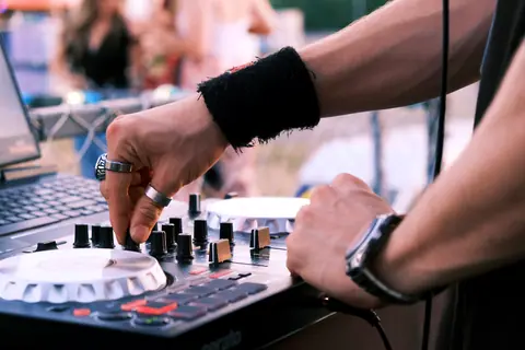 DJ mixing music outdoors at a lively daytime party, showcasing hands-on equipment.