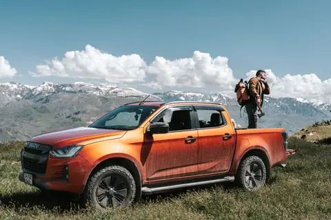 Explorer standing beside an orange pickup truck in scenic mountains, symbolizing freedom and adventure.