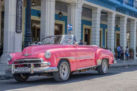 Vintage pink convertible car parked in front of historic hotel in La Habana, Cuba.