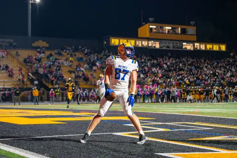 An excited football player celebrates a touchdown during a thrilling night game in a packed stadium.
