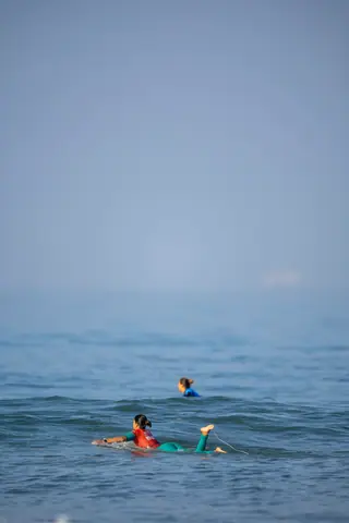 Two surfers paddle on their boards in the ocean, enjoying a sunny day.