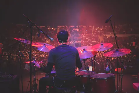 Back view of drummer playing on stage at a live music concert with a packed audience.