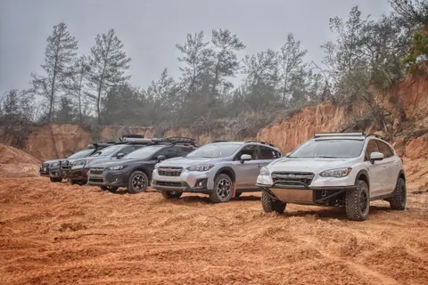 A row of SUVs parked on rough, dusty terrain with trees and a clay backdrop, showcasing adventure and ruggedness.