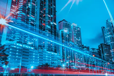 Colorful cityscape of illuminated skyscrapers and dynamic light trails at night.