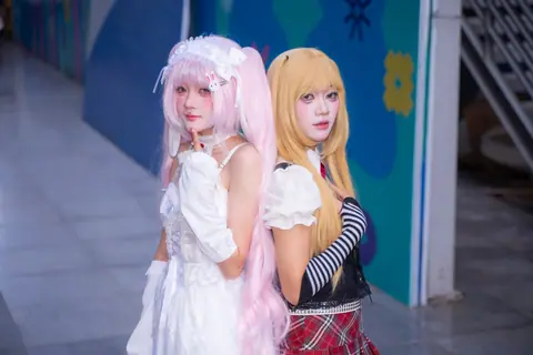 Two cosplayers in vibrant anime costumes posing indoors, showcasing creative character outfits.