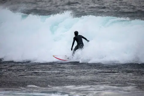 Surfer in wetsuit tackling Norway's icy waves in winter.