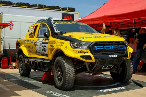 A vibrant yellow rally car on display at an outdoor racing event during the day.
