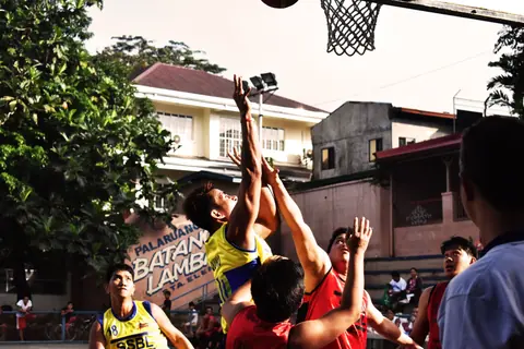A group of young adults energetically playing an outdoor street basketball game.