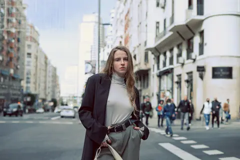 A young woman confidently poses in a bustling Madrid street, showcasing modern urban fashion.
