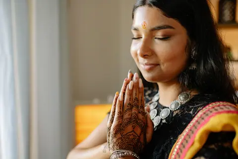 A woman in traditional Indian attire prays during Diwali, showcasing intricate henna designs.