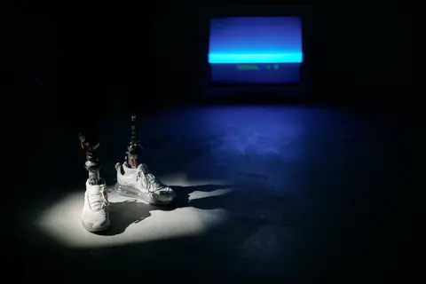 Futuristic prosthetic legs in sneakers illuminated by spotlight. Conceptual studio shoot with blue TV light.