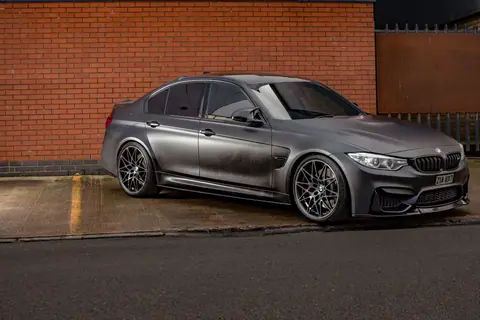 Stylish matt black BMW M3 parked outdoors against a classic brick wall in Birmingham.