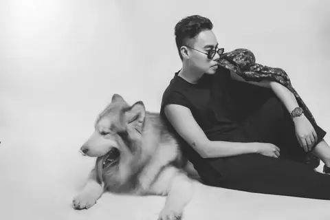 Stylish black and white studio portrait of a man in sunglasses with a large dog.