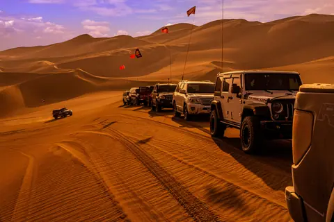 A convoy of off-road vehicles navigating through vast desert dunes during the day.