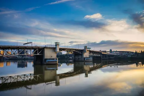 Modern bridge construction over calm river under colorful sky reflected in quiet water of canal
