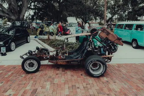 A rustic buggy on display at a vintage car show, showcasing automotive diversity in an urban setting.